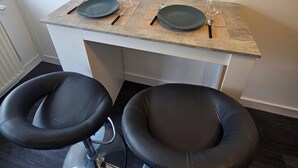 Un petit coin repas avec deux chaises noires et une table mise avec des assiettes, des verres et des couverts.