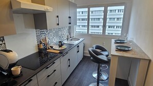 Une cuisine moderne avec un plan de travail noir, des meubles blancs et une fenêtre donnant sur des immeubles.