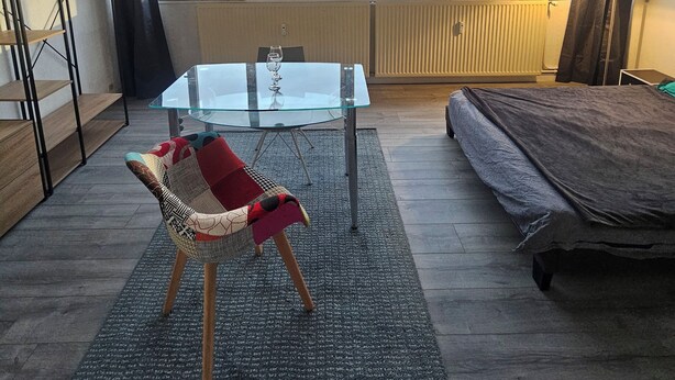 Une chambre moderne avec une table en verre, une chaise, un lit et de grandes fenêtres donnant sur la ville.