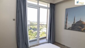 Una camera d'hotel con una grande finestra, un letto e un dipinto di una moschea sulla parete.