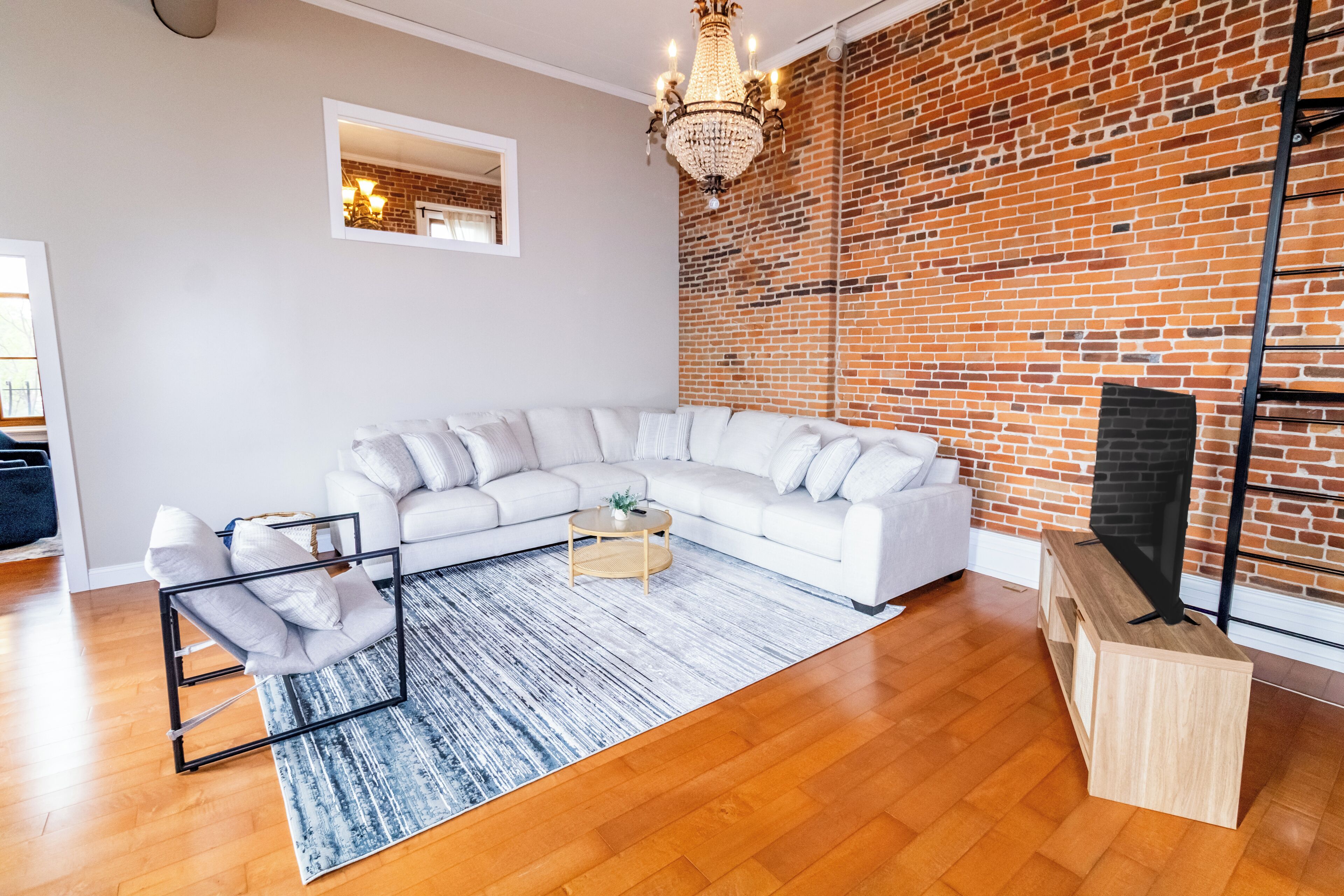 Een moderne woonkamer met een witte modulaire bank, een salontafel, een kroonluchter, een bakstenen muur en een tv-meubel.