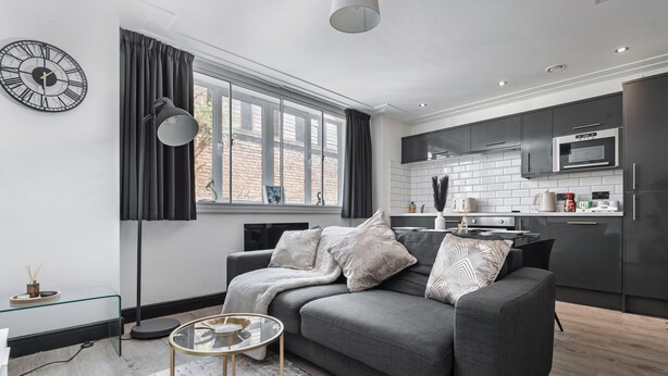 A modern living room with a grey sofa, a glass coffee table, and a black floor lamp.