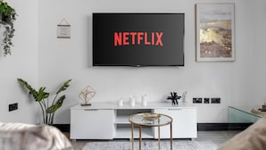 A modern living room with a large flat-screen TV mounted on the wall displaying "NETFLIX".
