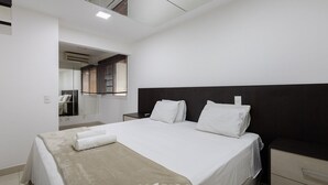 Una habitació d'hotel moderna amb un llit gran, una tauleta de nit, un mirall i una finestra amb persianes.