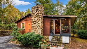 A rustic cabin with a stone chimney, a porch with outdoor seating, and a stone staircase leading to the entrance. - Cabin in the Clouds + Hot tub-close to everything! (Pigeon Forge)