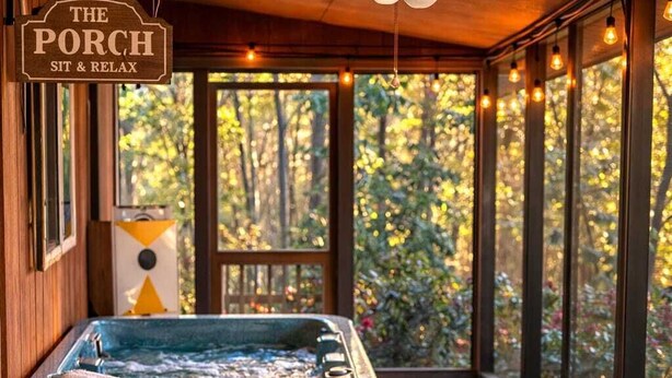 A wooden deck with a hot tub, a ceiling fan, and a sign reading 'The Porch Sit & Relax'. - Cabin in the Clouds + Hot tub-close to everything! (Pigeon Forge)