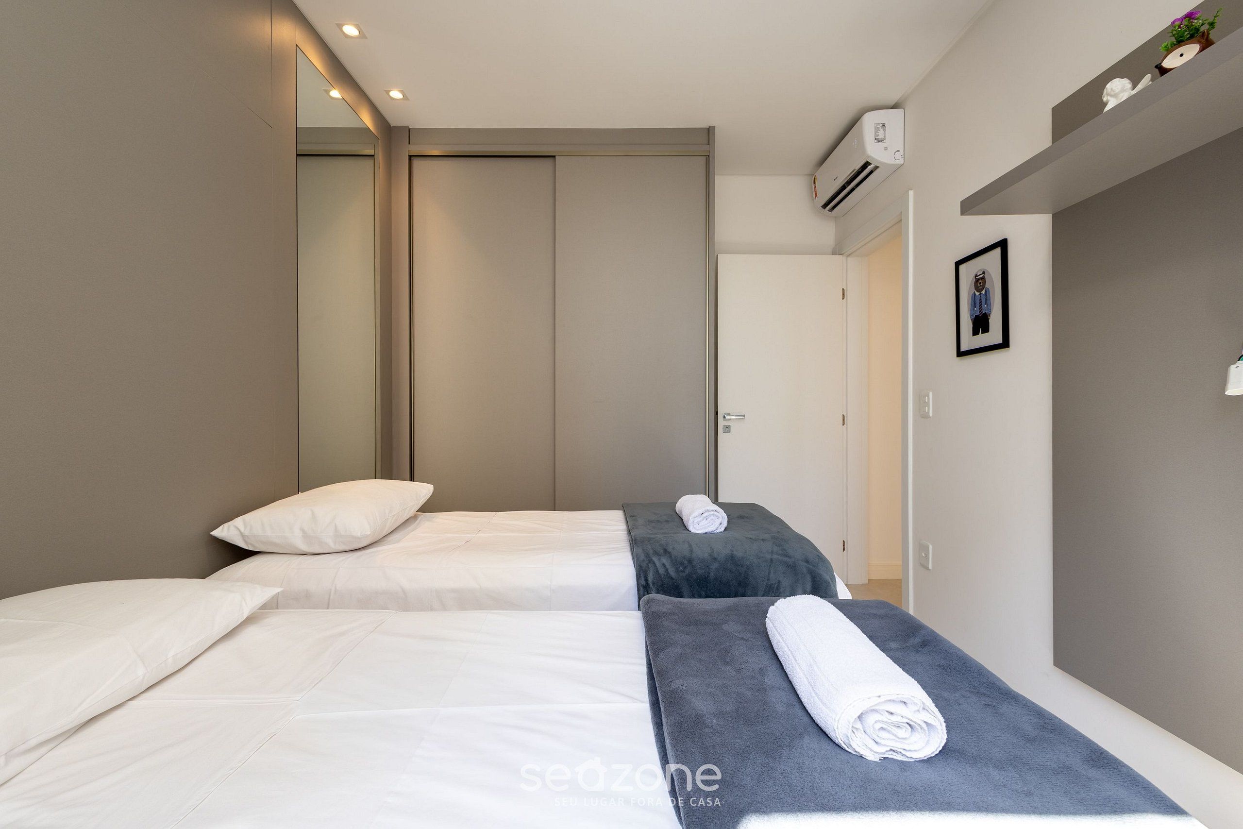 A modern hotel room with two beds, a large mirror, and a small shelf with decorative items.