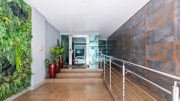 A modern interior with a wooden staircase, a green vertical garden, and a glass door leading to a car.