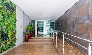 A modern interior with a wooden staircase, a green vertical garden, and a glass door leading to a car. - Apt w/ Gourmet Balcony 450m From Beach Reb0802 (Itapema)
