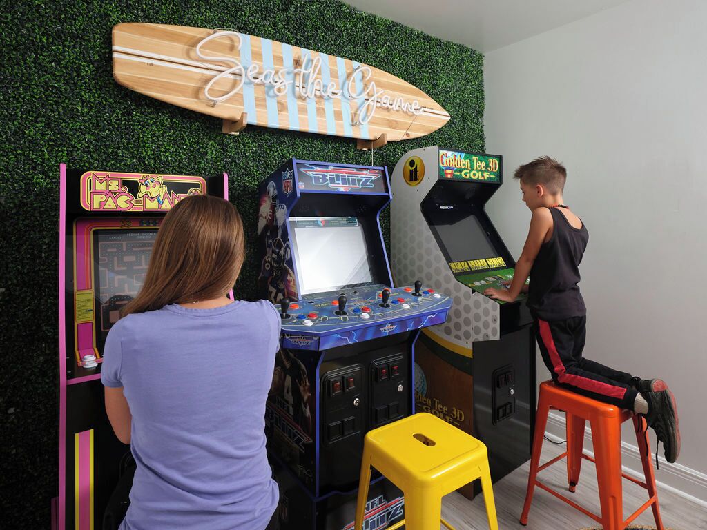 Ein Zimmer mit Spielhallenspielen, einem Surfbrett als Dekoration und einem gelben Hocker.