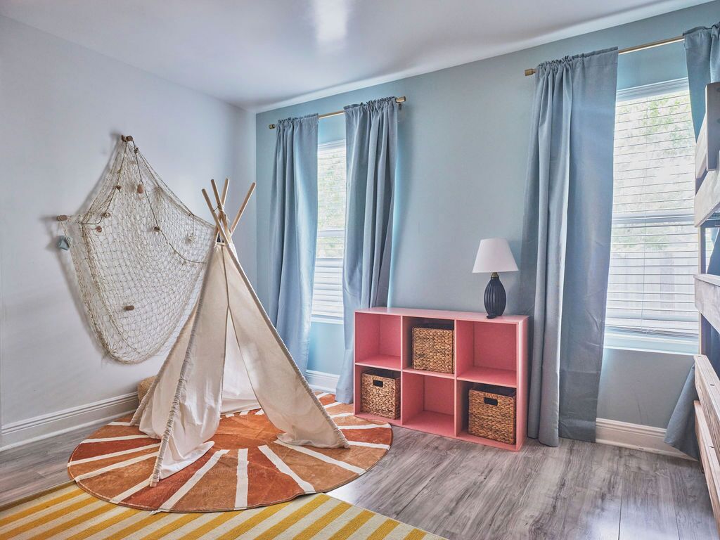 A room with a teepee, a pink shelf with baskets, and a lamp.