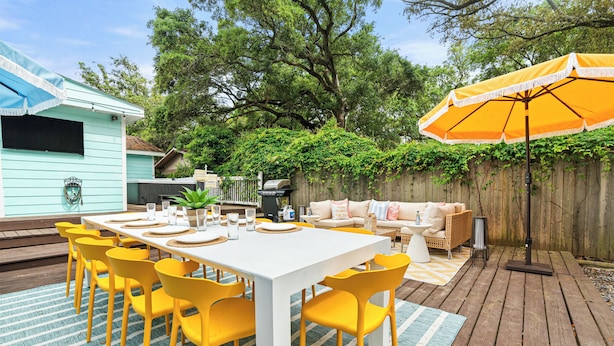 A patio with a white table, yellow chairs, and a wooden deck. - Pool, Hot Tub, Pickleball, Game Room & Spacious for Groups - Near Beach! (Gulfport)