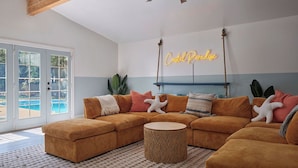A living room with a large sectional sofa, a round coffee table, and a neon sign reading "Crystal Paradise". - Pool, Hot Tub, Pickleball, Game Room & Spacious for Groups - Near Beach! (Gulfport)