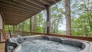 Un bain à remous installé sous une terrasse en bois, avec vue sur une forêt.