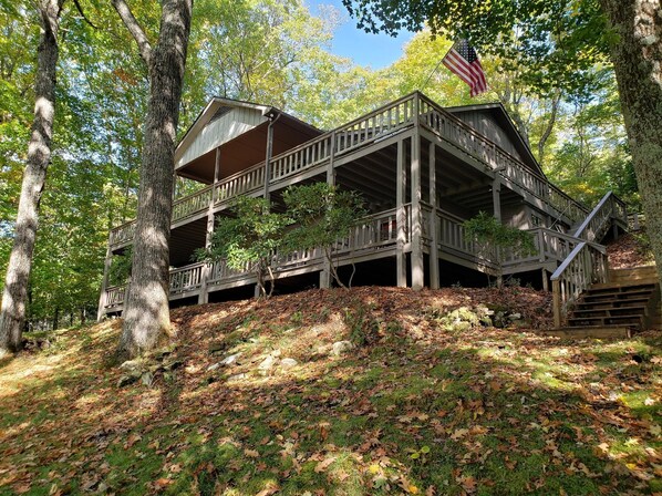 A wooden cabin with a balcony and a flag, surrounded by trees and a grassy hill. - Mountain Magic in the Wolf Laurel Community (Mars Hill)