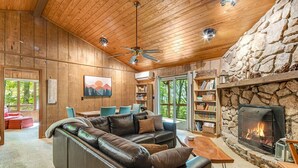 Un salon chaleureux avec un canapé en cuir, un plafond en bois, une cheminée en pierre et une bibliothèque.