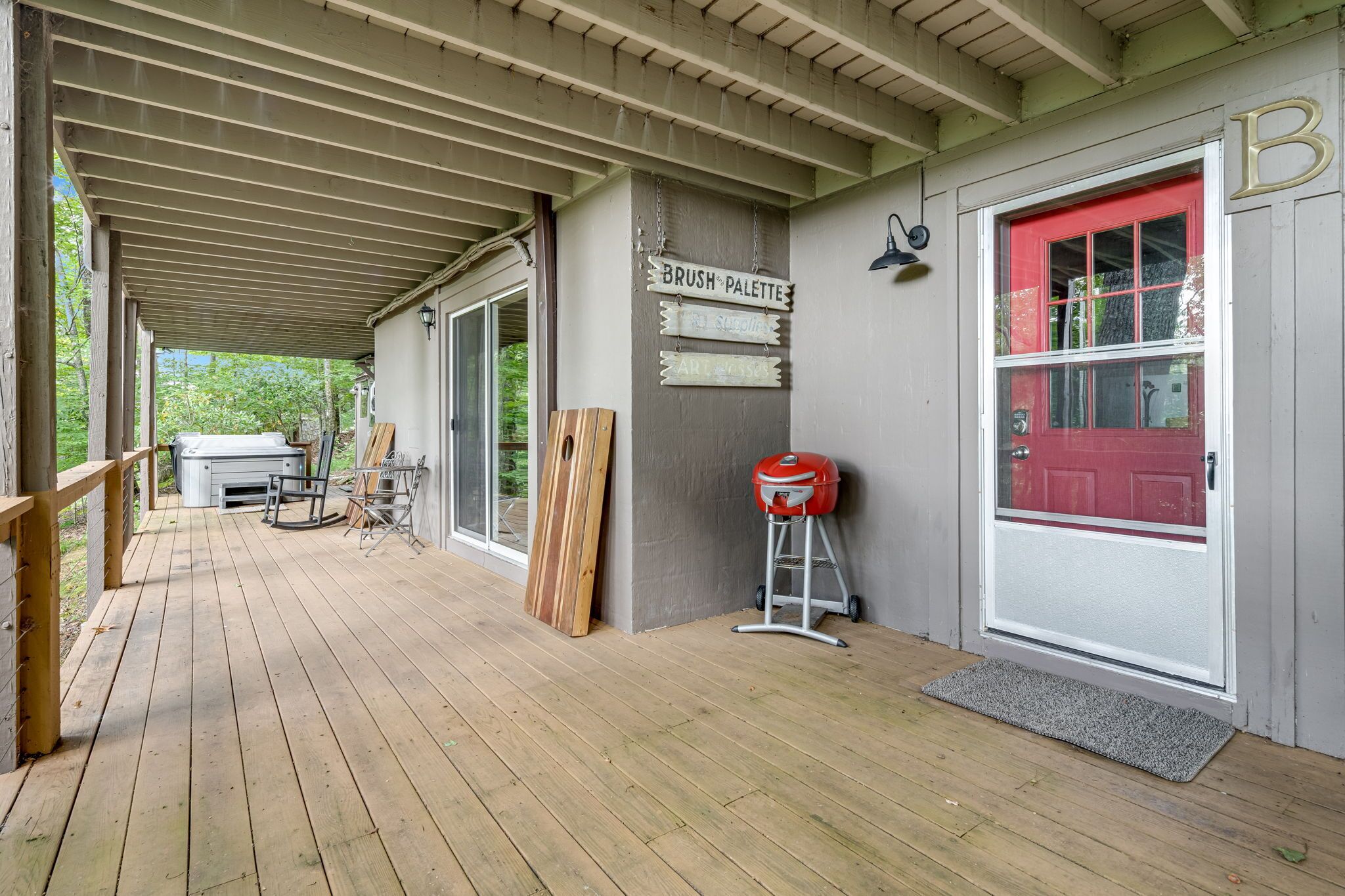 A covered porch with a wooden deck, a red door, and signs indicating a brush palette and art supplies.