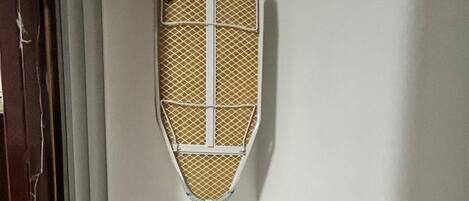 A room with a metal shelf, a wall-mounted ironing board, and a door with a metal handle.