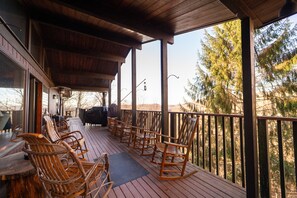 A wooden deck with outdoor seating and a view of trees. - Lovely Cabin - Sleeps 12 - Close to Hatley Pointe Ski Resort (Mars Hill)