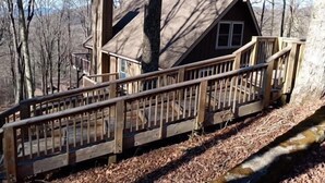 A wooden cabin with a staircase leading up to a deck, surrounded by trees. - Modern comfort with mountain charm! (Mars Hill)