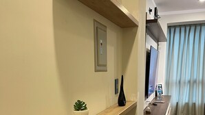 Ein Flur mit einem Holzbodenregal, einer Topfpflanze, einem an der Wand montierten Lichtschalter und einem Fernseher auf einem Sockel.