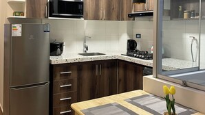 Eine moderne Küche mit Holzschränken, einem Edelstahlkühlschrank, einer Mikrowelle und einem Spülbecken. Ein Fenster bietet einen Blick nach draußen.