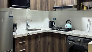 Eine moderne Küche mit Holzausstattung, einem Edelstahlkühlschrank, einer Mikrowelle, einem Wasserkocher und einem Geschirrspüler.