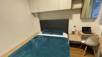 Une chambre à coucher avec un lit, un bureau avec un ordinateur portable et une chaise.