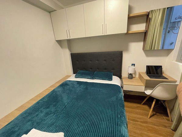 Un dormitorio con cama, escritorio, laptop y silla.