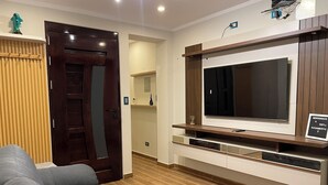 Ein modernes Wohnzimmer mit grauem Sofa, Holzboden, einem großen Fernseher auf einem Holztisch und einer Tür mit Spiegel.