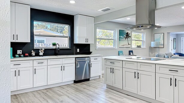 Een moderne keuken met witte kastjes, een RVS vaatwasser en een raam met uitzicht op een huis.