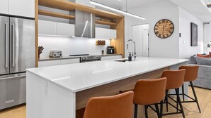 A modern kitchen with a large island, stainless steel appliances, and a wooden accent wall. - The Axia at Verbier: Hot Tub, Sauna, Seasonal Pool (Mont-Tremblant)