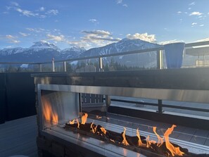 A rooftop bar with a glass enclosure, a fire feature, and a view of snow-capped mountains. - Mackenzie Mountain Hop | Home for 6 in Revelstoke (Revelstoke)