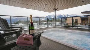 Ein Whirlpool auf dem Dach mit Blick auf schneebedeckte Berge, eine Flasche Moët & Chandon Champagner und ein rosafarbenes Handtuch auf einem Stuhl.