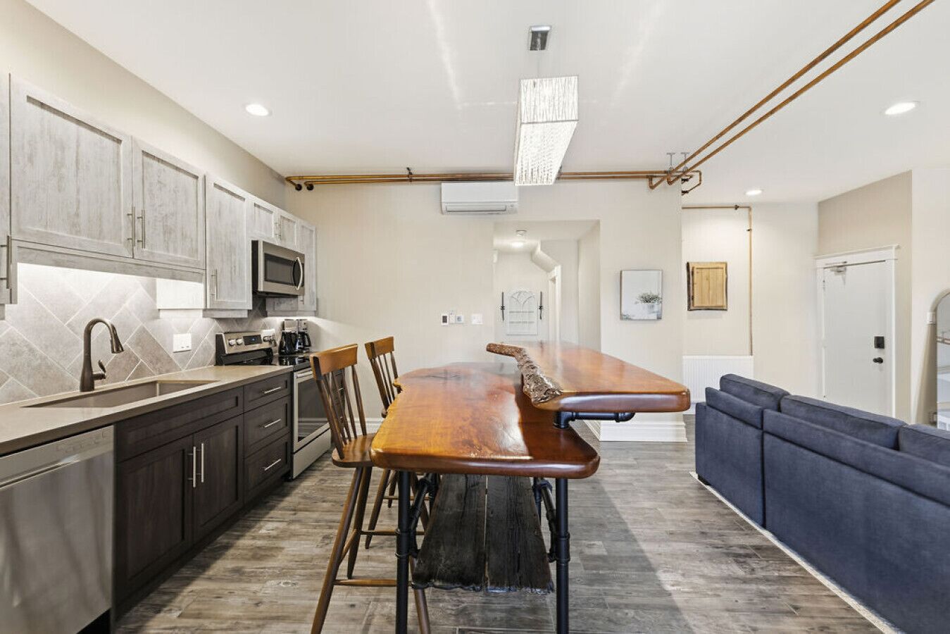 A modern kitchen with a long wooden bar counter, dark cabinets, and a microwave.