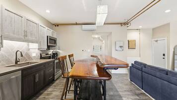 A modern kitchen with a long wooden bar counter, dark cabinets, and a microwave.