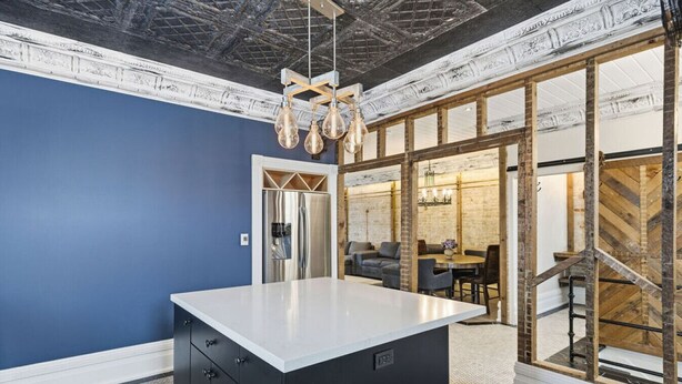 A modern kitchen with a central island, a dining area with a herringbone-patterned wall, and a staircase leading to an upper level.