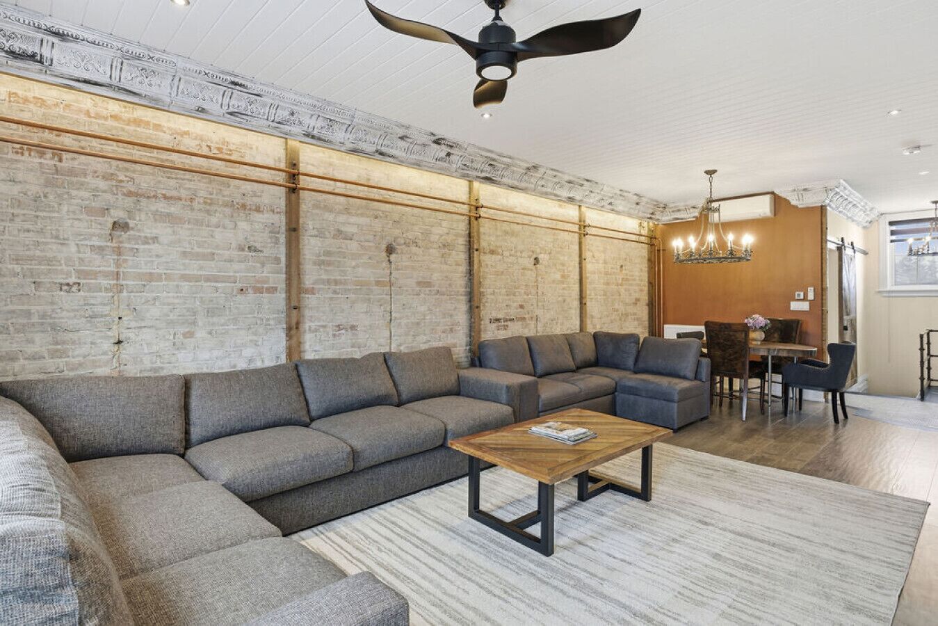 Un salon moderne avec un canapé d’angle, une table basse en bois et un coin repas agrémenté d’un lustre.