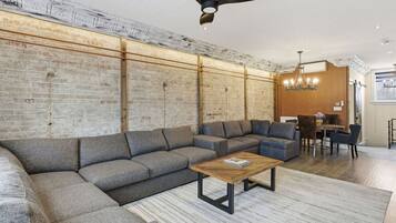 Un salon moderne avec un canapé d’angle, une table basse en bois et un coin repas agrémenté d’un lustre.