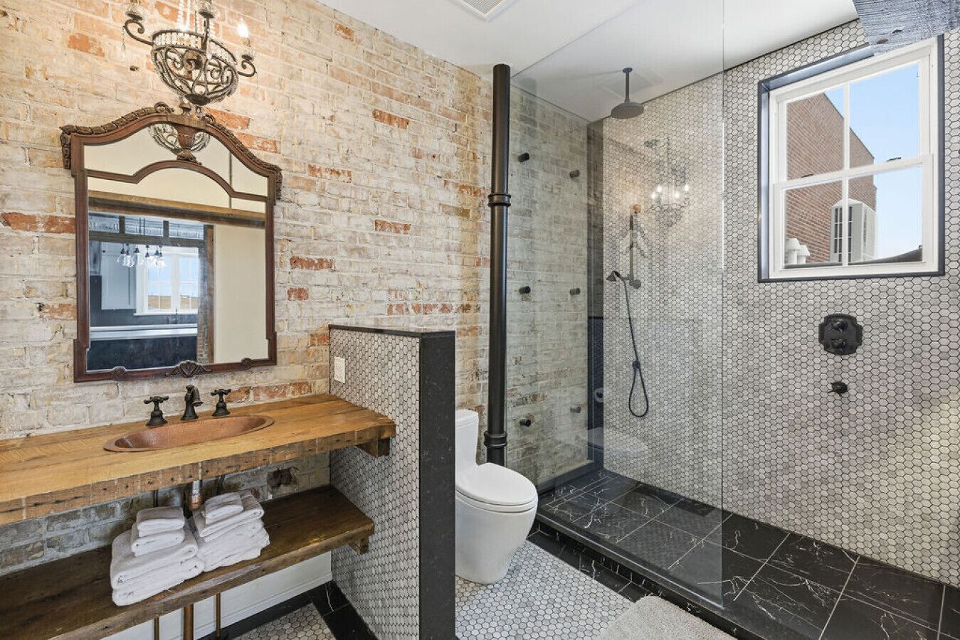 A bathroom with a brick wall, wooden vanity, and a shower area with a glass door.