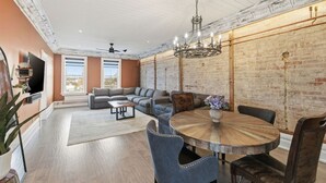 A modern living room with a sectional sofa, a round dining table, and a brick wall.