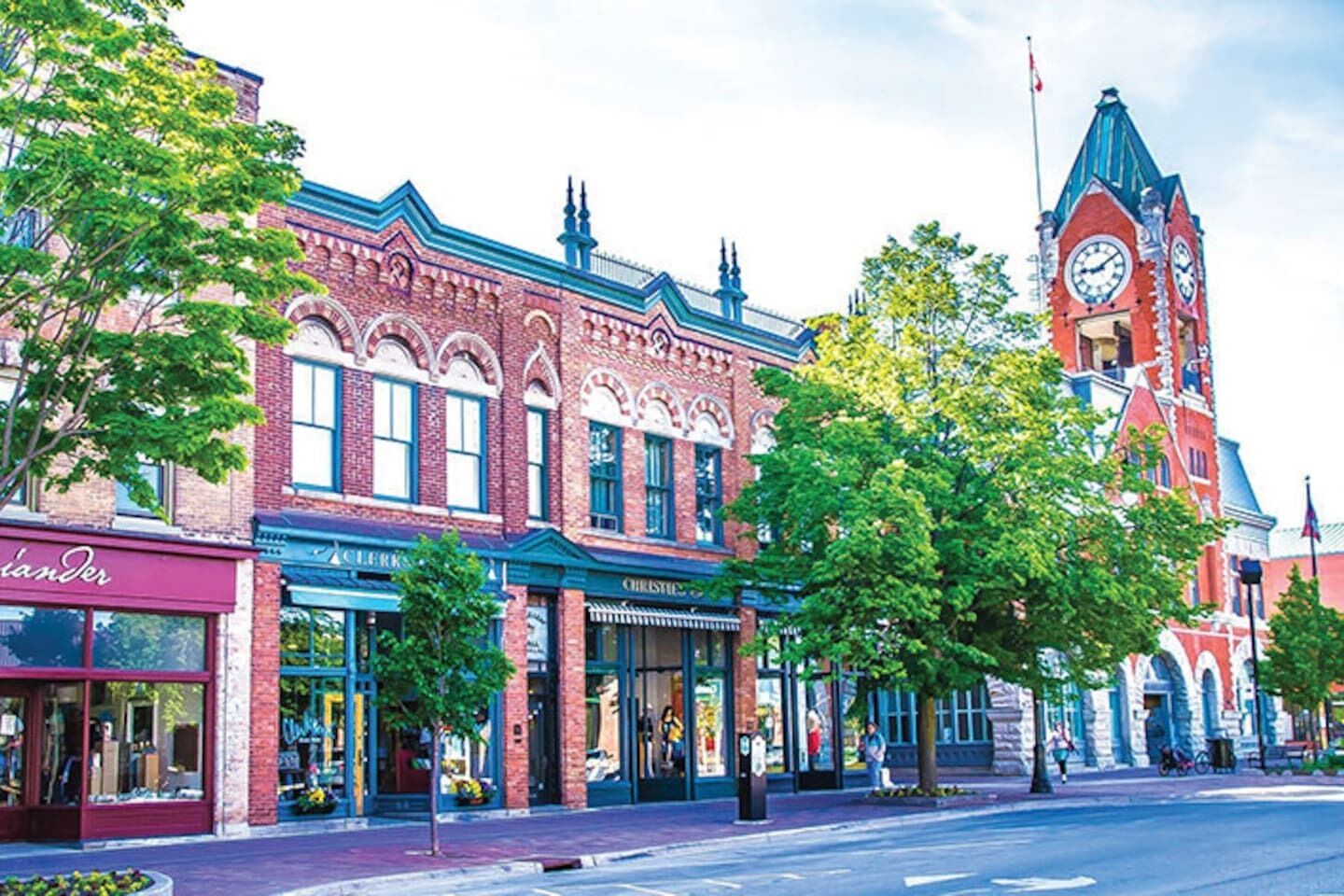 A historic building with a clock tower, storefronts, and a street with trees.