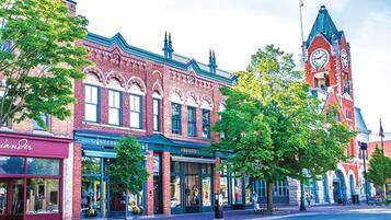 A historic building with a clock tower, storefronts, and a street with trees.