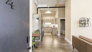 Une cuisine moderne dotée d’un îlot central, un coin repas avec une table et des chaises, et un couloir menant à une salle de bain.