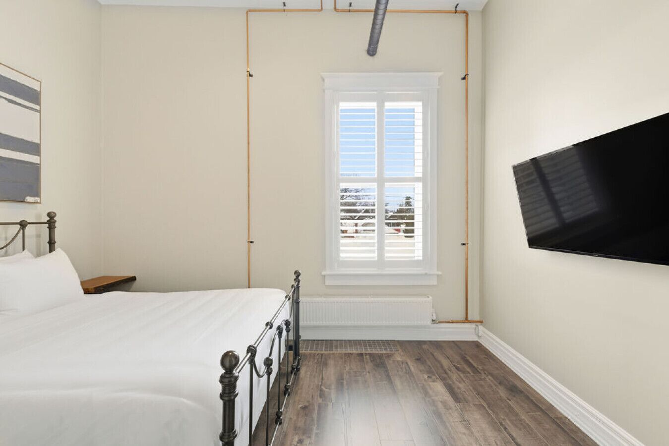A bedroom with a bed, a window, a radiator, and a TV mounted on the wall.