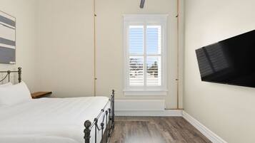 A bedroom with a bed, a window, a radiator, and a TV mounted on the wall.