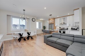 A modern kitchen with white cabinets, a stainless steel refrigerator, and a dining area with a white table and chairs. - Splendid Home in Victoria (Langford)