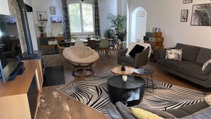 A modern living room with a sofa, armchair, and coffee table. There is a fireplace, dining area, and kitchen visible in the background. - Large Provençal-style family home with swimming pool in a quiet location (Saint-Maximin-la-Sainte-Baume)