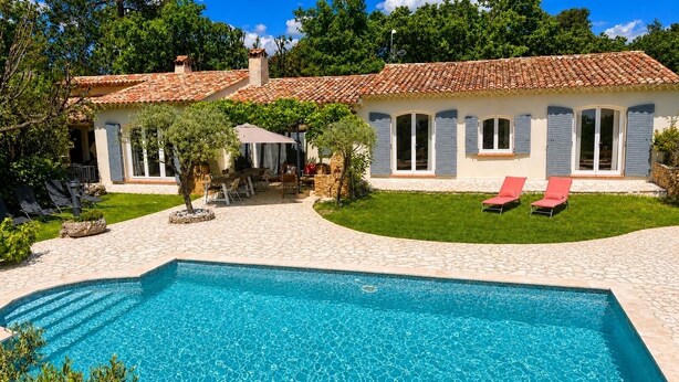A swimming pool with a tiled deck, a covered patio, and a house with a tiled roof and shutters. - Large Provençal-style family home with swimming pool in a quiet location (Saint-Maximin-la-Sainte-Baume)