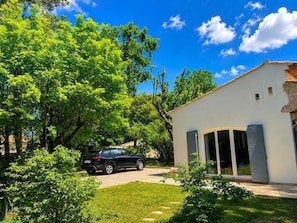 Une maison moderne avec une voiture garée dans l’allée, entourée d’une végétation luxuriante et sous un ciel bleu dégagé.